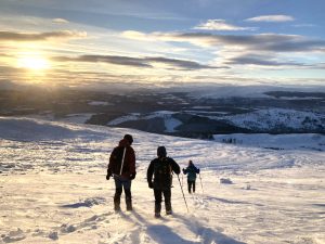 Three walkers on a snow covered mountain, with the sun setting