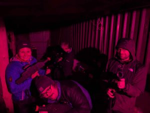 4 people outdoors at night, ready to play laser tagging, bathed in reddish light
